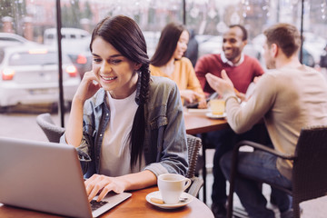 Online news. Pleasant joyful pretty woman resting at cafe while grinning and staring at the screen