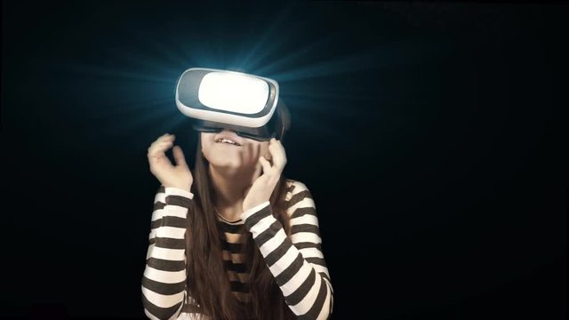 Teenager caucasian girl looking at Virtual Reality Glasses which glowing by blue misterious light and gesturing with her hands with many different emotions from fear to amazement.