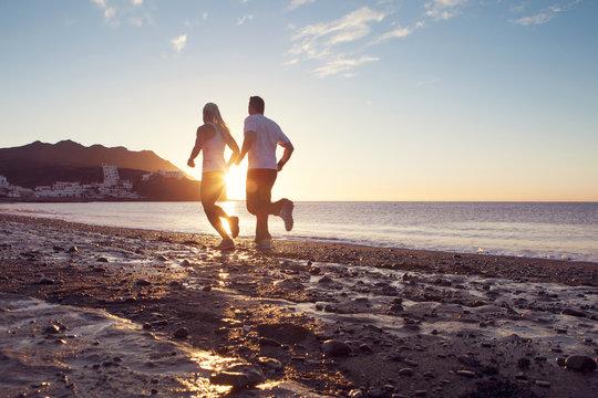 Kvinna och man springer på stranden i soluppgången