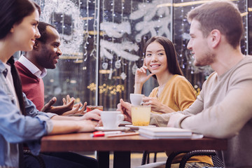 Time with friends. Joyful positive four friends smiling while talking and sitting at cafe