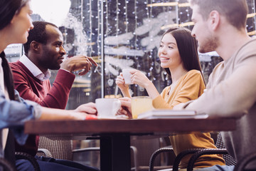 Secrets between friends. Low angle of happy merry four friends sitting at the table while enjoying time together and gossiping