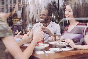 Great news. Nice young three friends talking while enjoying salad and sitting at the table