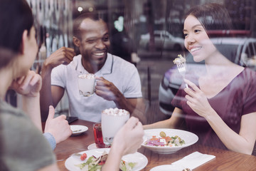 Tasty food. Joyful sincere four friends enjoying meal while smiling and sitting at the table