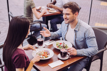 Lovely conversation. Optimistic vigorous young couple chatting while eating salads and man explaining his point of view