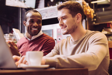 Best colleague. Smart joyful two colleagues working together while Afro American man grinning and staring at his colleague
