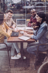 Team work. Energetic positive four colleagues debating while working on team report and sitting at cafe