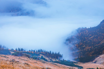 mountain landscape with fog below the peaks and clouds above them in blue tones