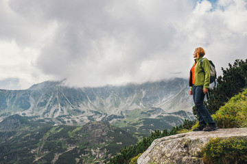 woman stands on the cliff and looks at the tops of mountains
