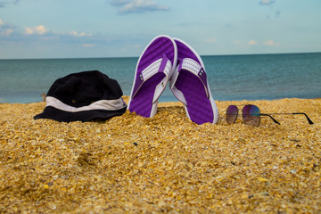 Pair of flip flops, hat and sunglasses on a sandy sea beach