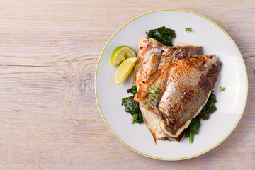 Roasted sea bream with spinach. Dorado or dorada fish fillet on white plate