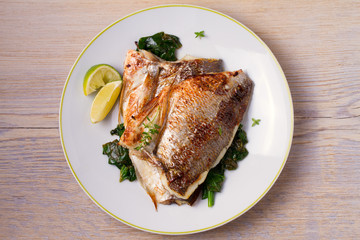 Roasted sea bream with spinach. Dorado or dorada fish fillet on white plate