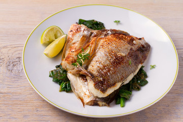 Roasted sea bream with spinach. Dorado or dorada fish fillet on white plate