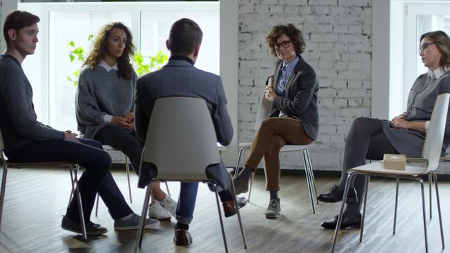 Wide shot of group of patient talking to mal psychotherapist during interpersonal therapy session