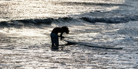 Surfer attaches his surfboard by leash (leg rope).