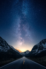 Fototapeta Milky way glowing above a road leading to distance in a mountain valley. obraz