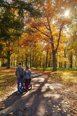 Jesienny krajobraz - park skąpany w ciepłym świetle, spacer pary młodych rodziców pchających alejką parkową wózek z dzieckiem © Wojciech