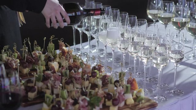 The waiter pours the champagne into the glasses. Table top full of glasses of sparkling white wine with bottles in the background.