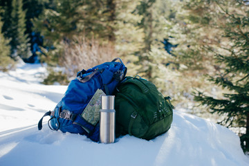 Two sports backpacks, a thermos, a map on the background of a winter forest