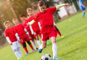 Fotobehang Boy kicking football on the sports field © Dusan Kostic