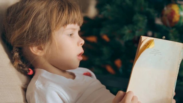 Small girl reading a book in front of Christmas tree