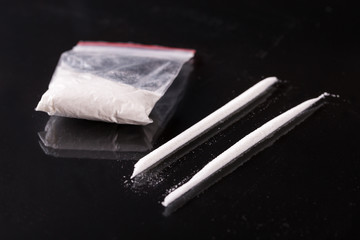 Two lines and plastic packet with cocaine on black background