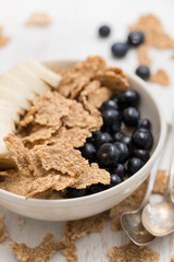 flakes with blueberries and banana on brown bowl on wooden background