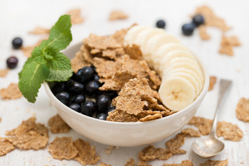 flakes with blueberries and banana on brown bowl on wooden background