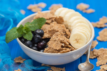 flakes with blueberries and banana on brown bowl on wooden background
