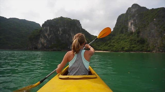 Woman exploring calm tropical bay with limestone mountains by kayak. Ha Long Bay, Vietnam