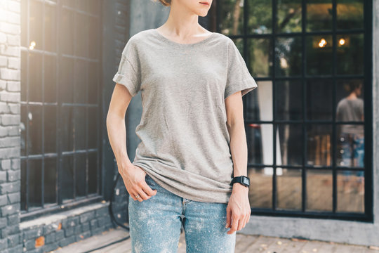 Summer day. Front view. Young millennial woman dressed in gray t-shirt is stands on city street. Mock up. Space for logo, text, image. Instagram filter, film effect, bokeh effect.