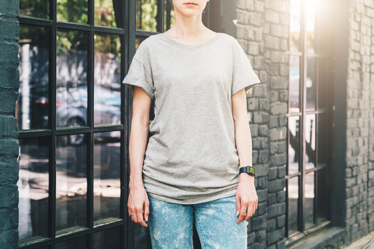 Summer day. Front view. Young millennial woman dressed in gray t-shirt is stands on city street. Mock up. Space for logo, text, image. Instagram filter, film effect, bokeh effect.