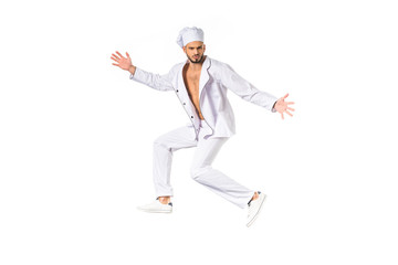 handsome young chef in uniform jumping and looking at camera isolated on white