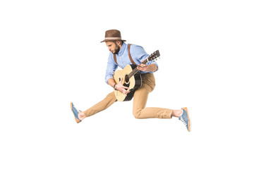 handsome young musician in hat playing guitar while jumping isolated on white
