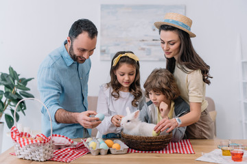 Young family preparing for easter holiday with bunny sitting in basket on table