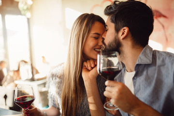 Close-up of an attractive couple. Boyfriend kissing his girlfriend in nose. Couple drinking red wine and celebrating anniversary or Valentine's day.