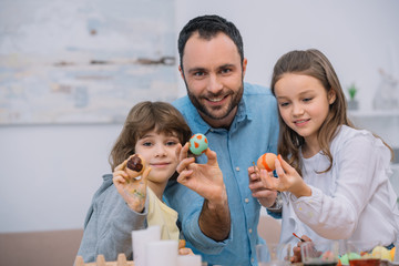 father and kids showing easter eggs at camera