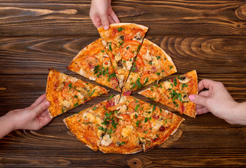 Hands taking pizza slices from wooden background.