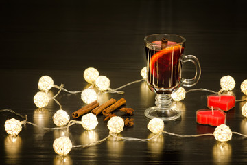 Mug of mulled wine with spices, candles in the shape of a heart and lanterns. Black background