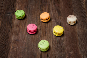 Six multicolored macarons on a brown wooden table. Top view