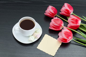 Fototapeta na wymiar Mug of coffee, blank postcard and pink tulips. Black background.