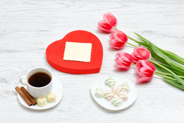 Fototapeta na wymiar Pink tulips, mug of coffee and marshmallow. Red heart shaped gift box. Clean postcard