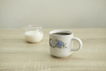 Fototapeta na wymiar ROSE CERAMIC COFFEE CUP Small rose ceramic coffee cup with milk jar on a wood table.