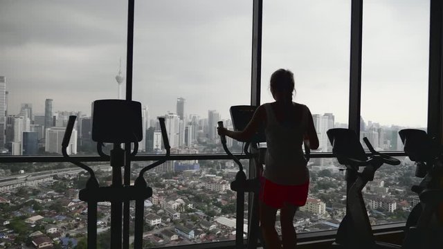 Young woman working out hard in sports club.Attractive girl at the gym riding on the spinning bike with great view over city.Active, healthy lifestyle and loosing weight concept.