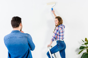 smiling girlfriend painting wall and looking at boyfriend