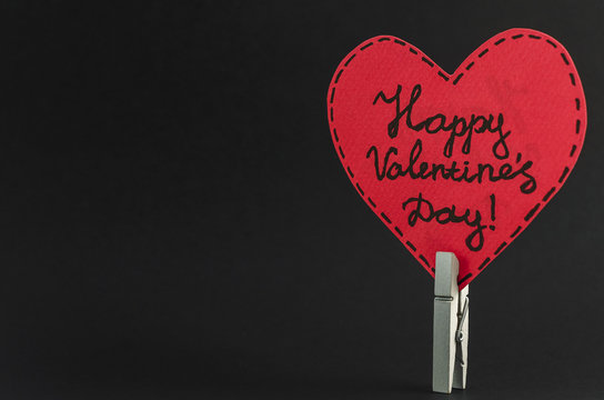Red heart on the clothespin with the greeting happy Valentines day on dark background.