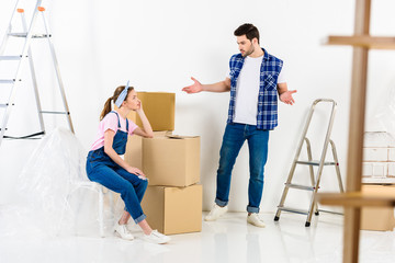 boyfriend showing shrug gesture and looking at girlfriend sitting on boxes