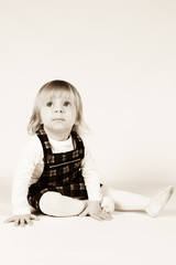 Naklejka premium Little blonde toddler girl with big Blue Eyes in red dress looking up.Sitting on the floor, white background. Portrait, close-up isolated , Sepia Tone