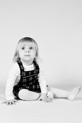Naklejka premium Little blonde toddler girl with big Blue Eyes in red dress looking up.Sitting on the floor, white background. Portrait, close-up isolated , Black and White photo