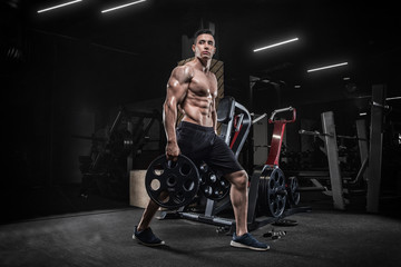 Fototapeta na wymiar A young male bodybuilder does exercises with sports equipment, makes sit-ups with a barbell, in a modern gym. Weightlifting. On a dark background.