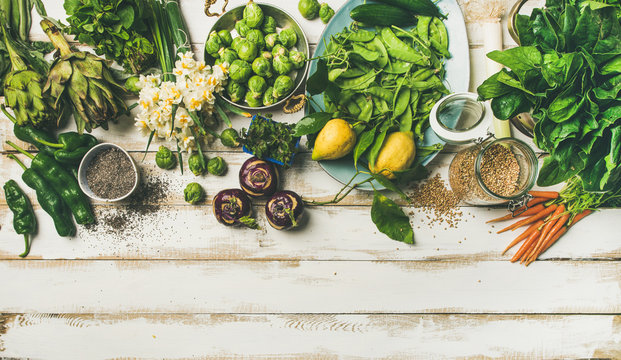 Spring healthy vegan food cooking ingredients. Flat-lay of vegetables, fruit, seeds, sprouts, flowers, greens over white wooden background, top view, copy space. Clean eating, diet food concept